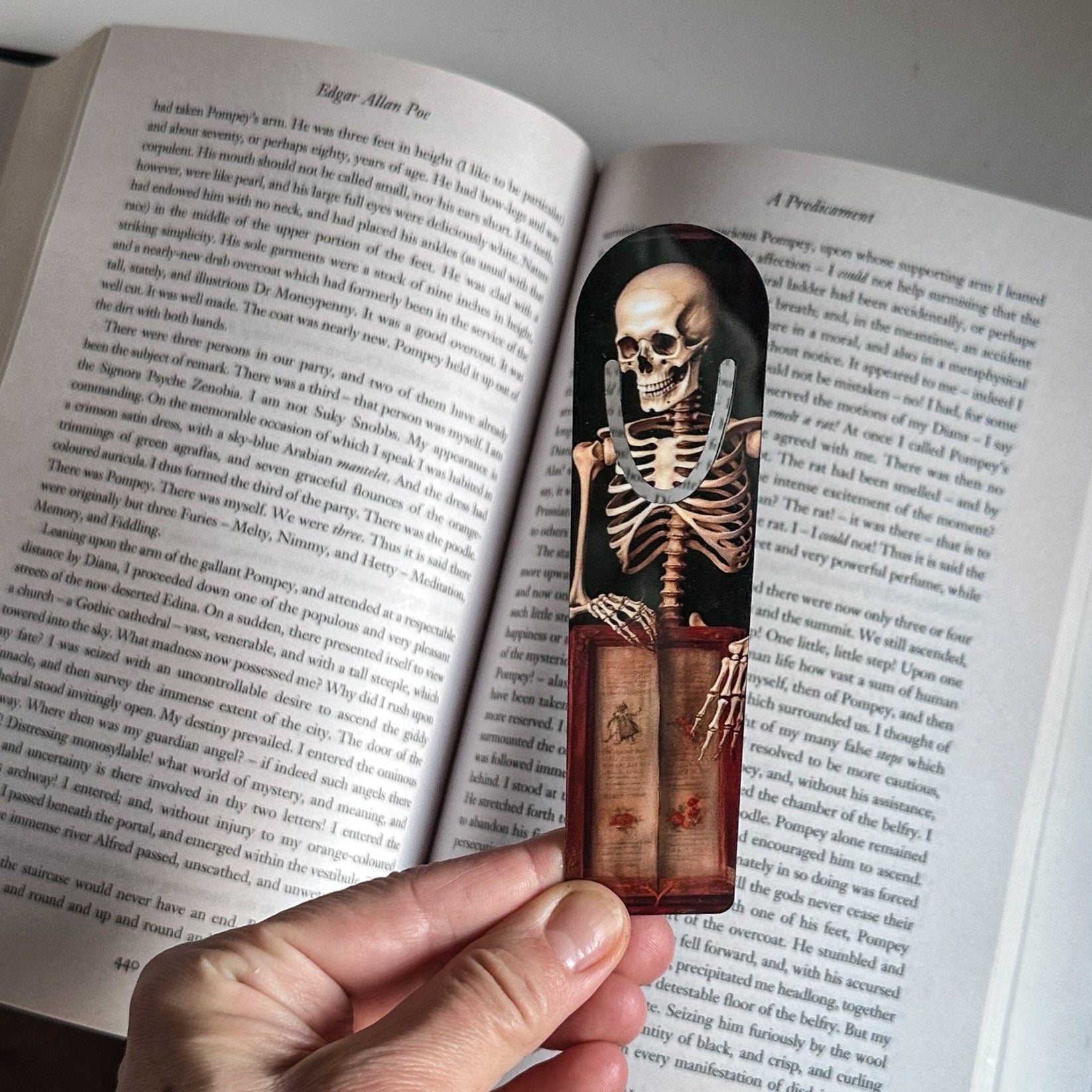 Skeleton with the Book metal bookmark held up beside an open book