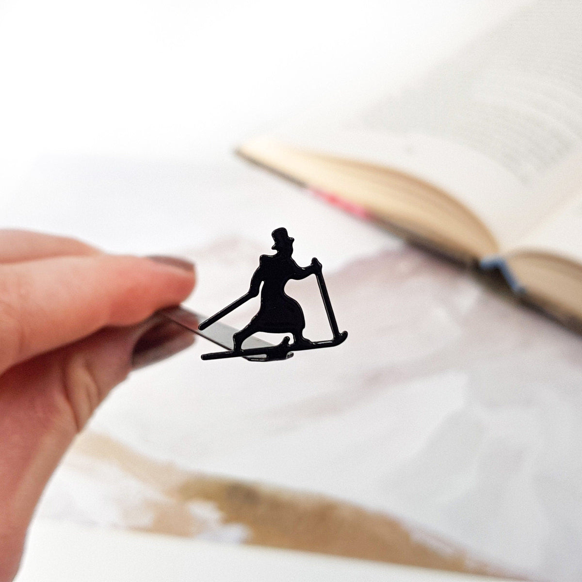 Skier in High Hat metal bookmark held in a hand above an open book