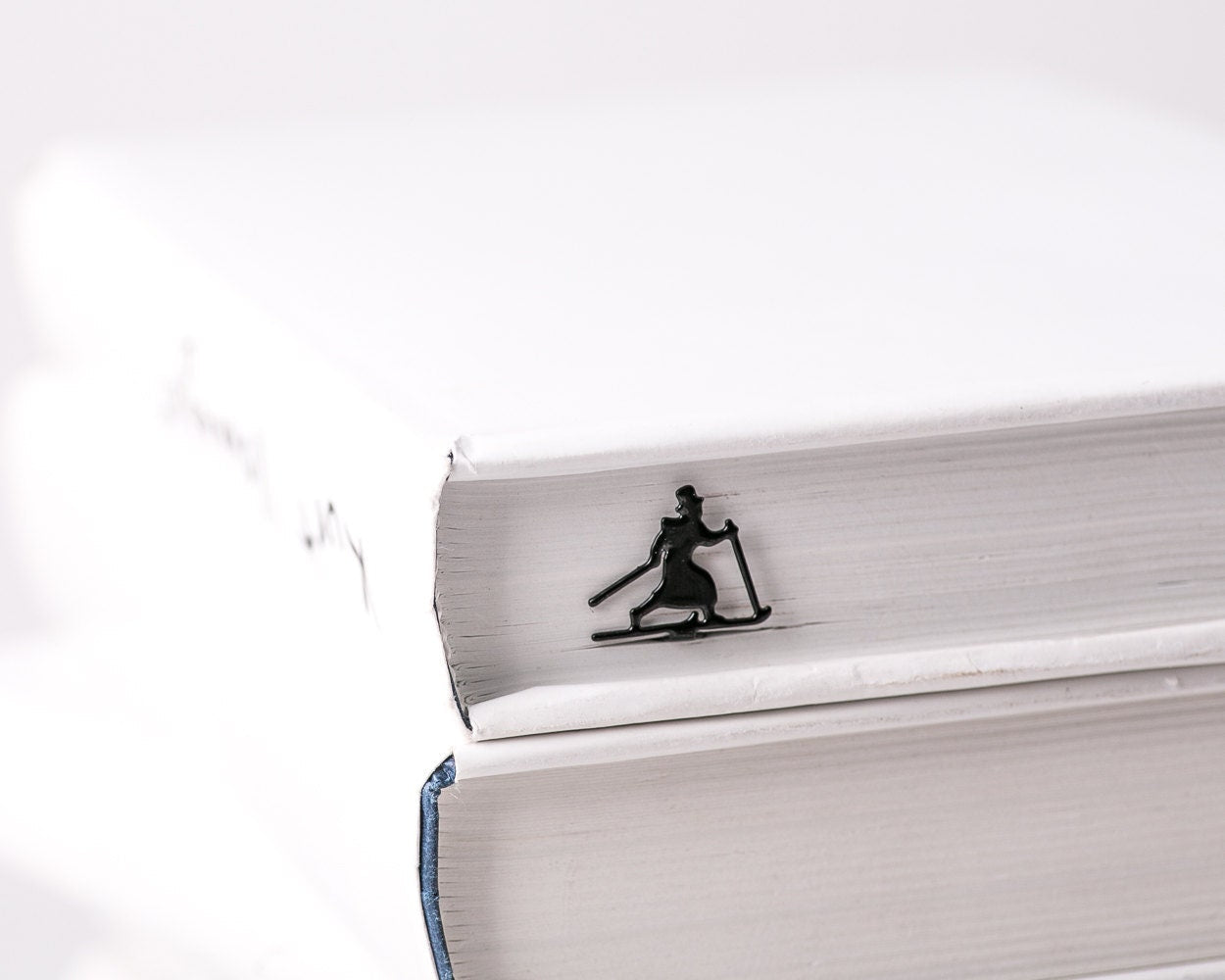 Skier in High Hat metal bookmark in a closed book, only its top showing above the pages