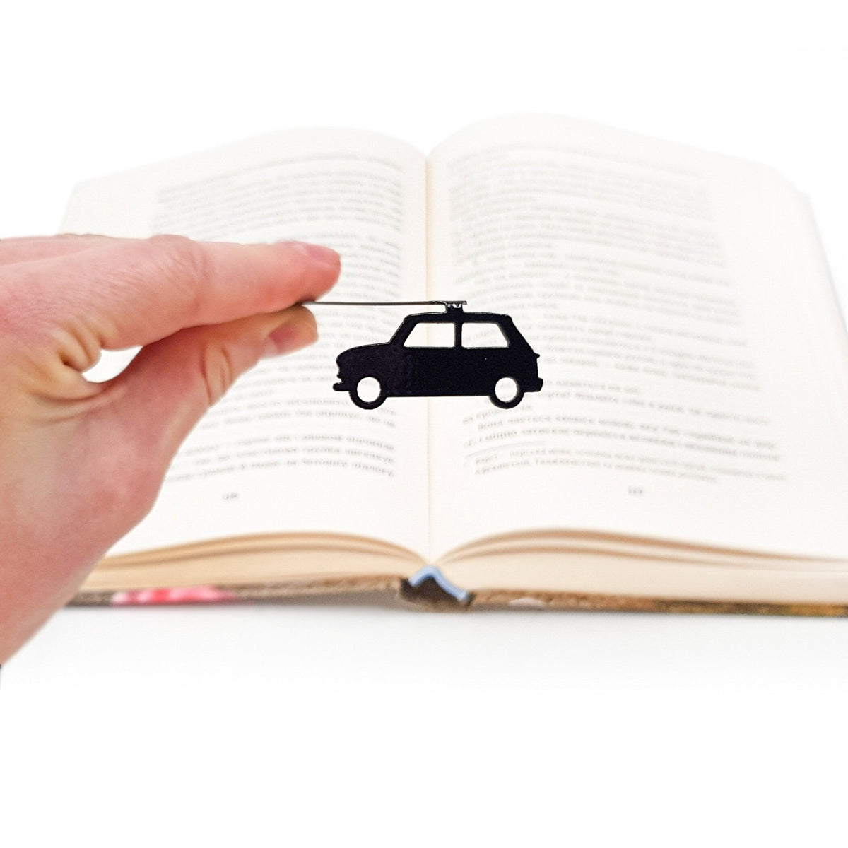 Black Car metal bookmark held in a hand above an open book