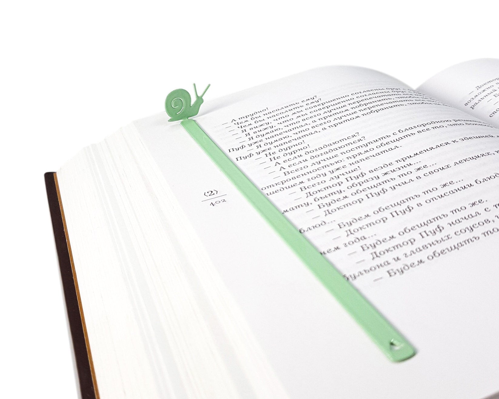 Snail metal bookmark in green resting on the pages of an open book