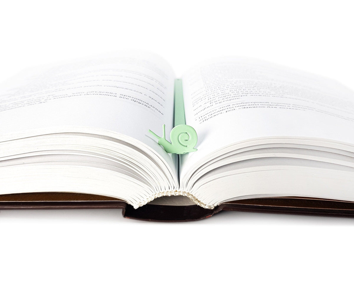 Snail metal bookmark in green marking a page in an open book