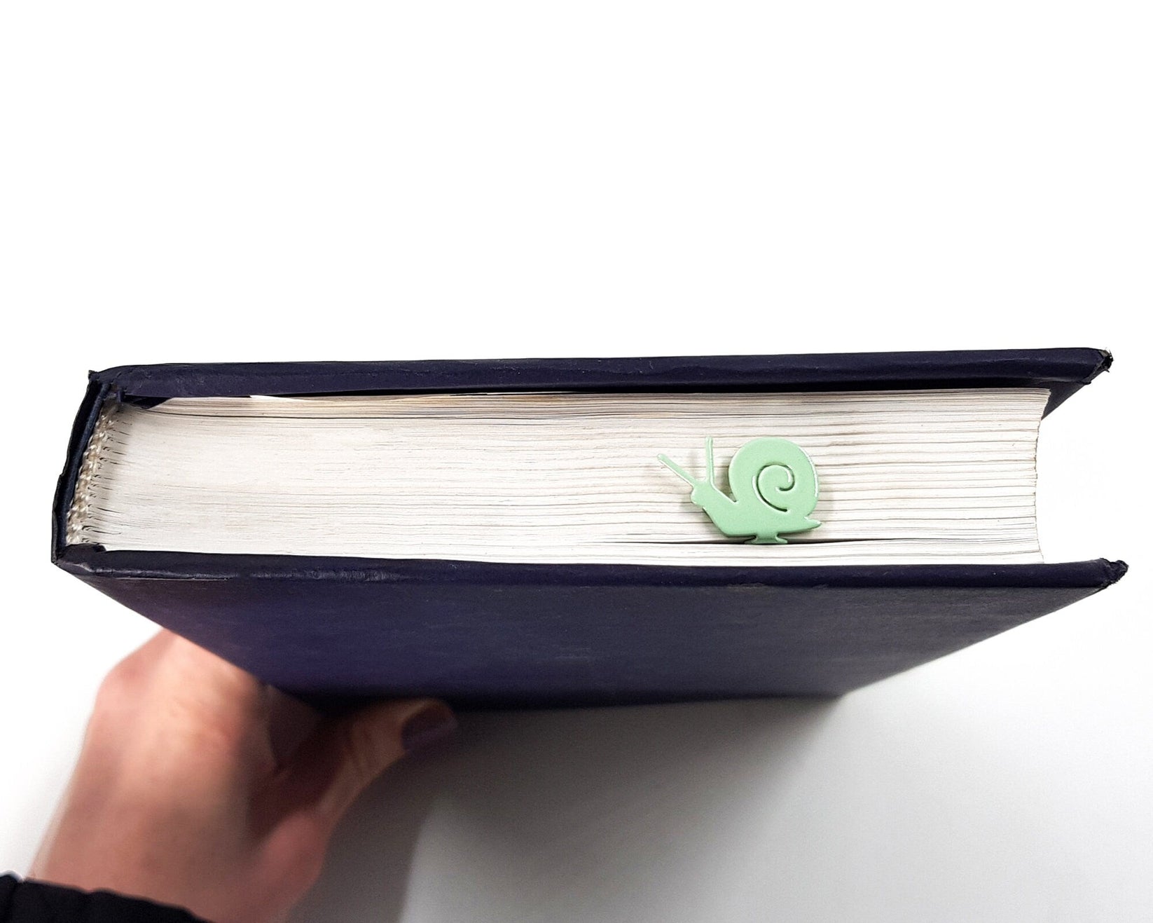Snail metal bookmark in green held in a hand above an open book
