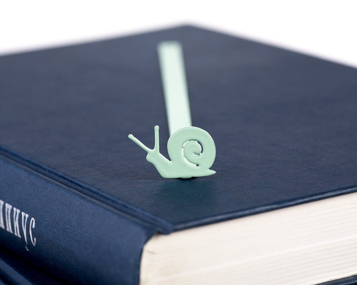 Snail metal bookmark in green in a closed book, only its top showing above the pages