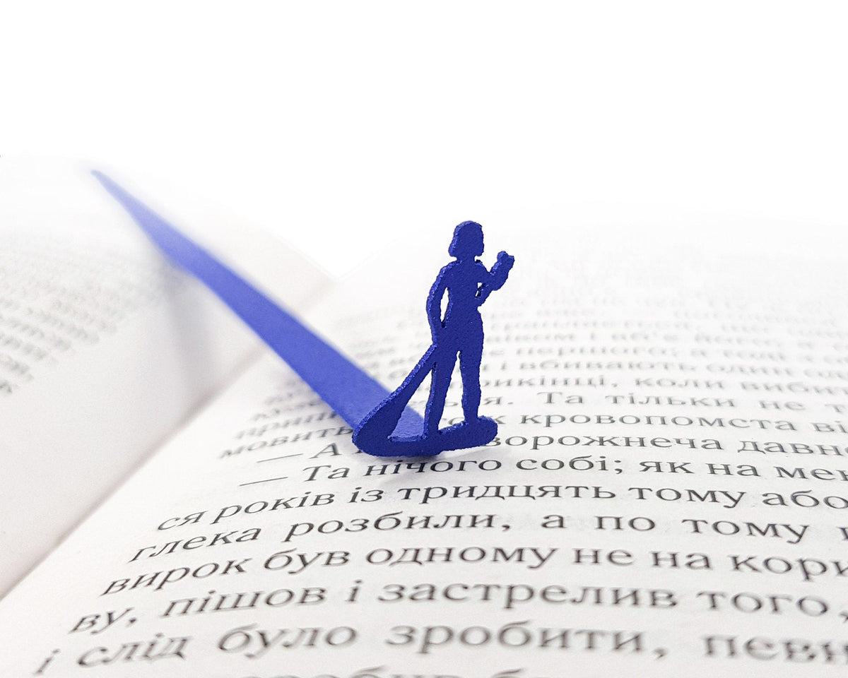 Surfer metal bookmark in blue resting on the pages of an open book
