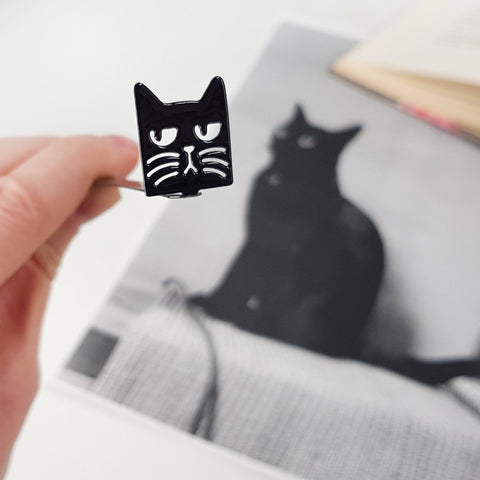 Suspicious Cat metal bookmark marking a page in an illustrated book