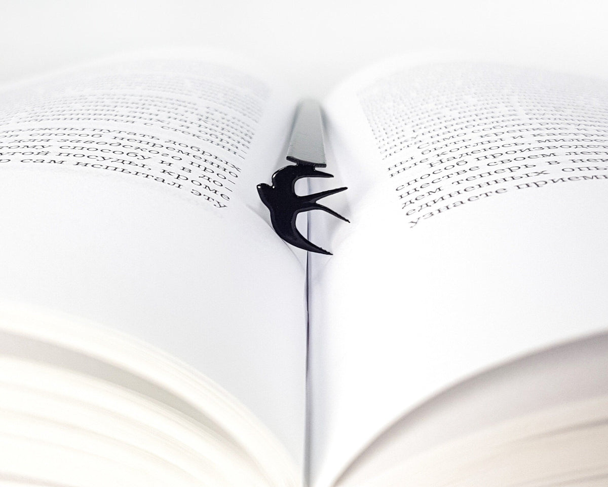 Swallow metal bookmark marking a page in an open book