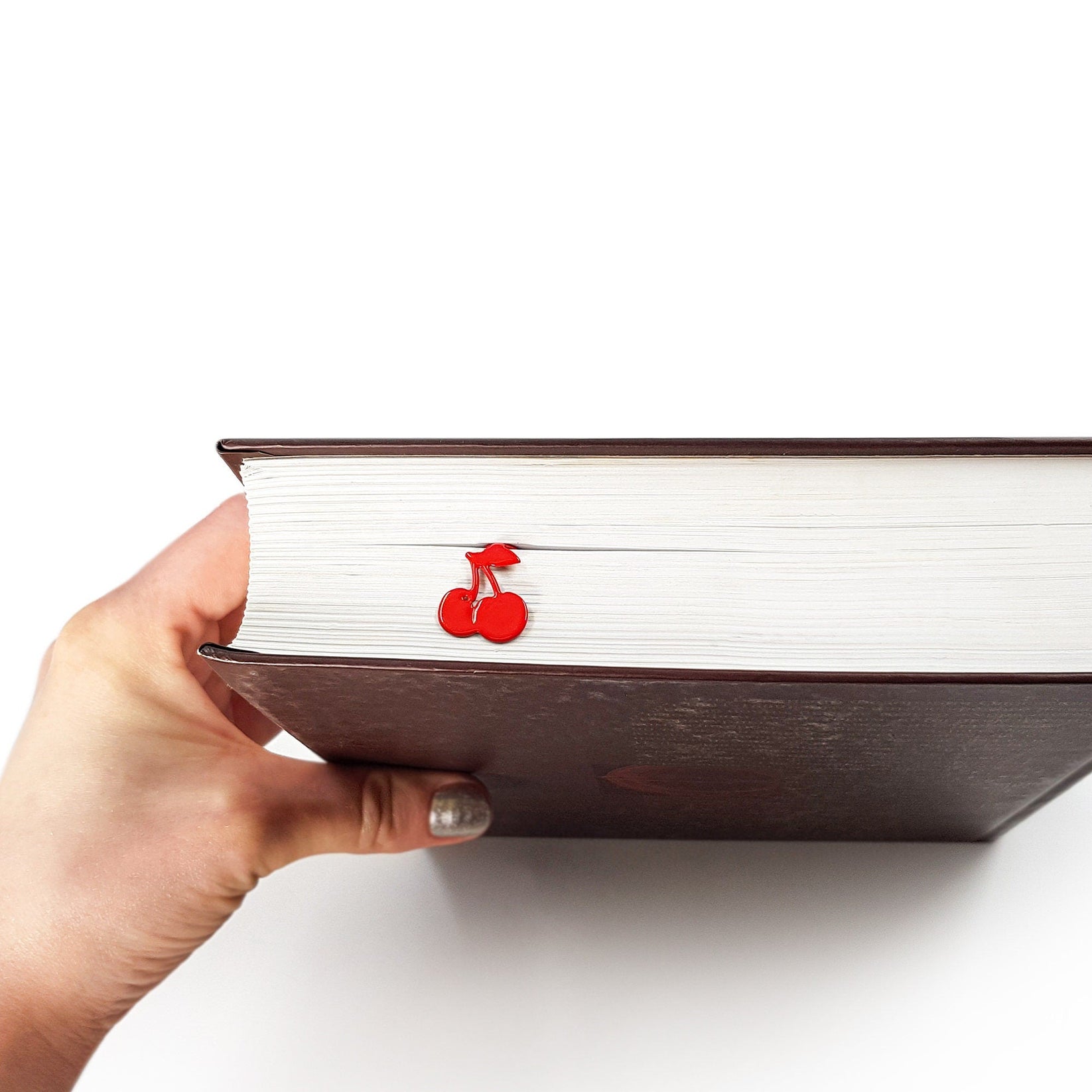 Sweet Cherries metal bookmark in red held in a hand above an open book