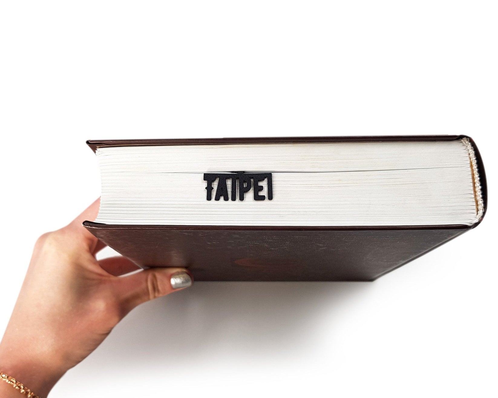 Taipei metal bookmark held up beside an open book