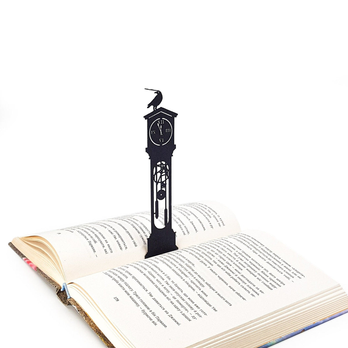 The Raven's Pendulum Dance metal bookmark resting on the pages of an open book