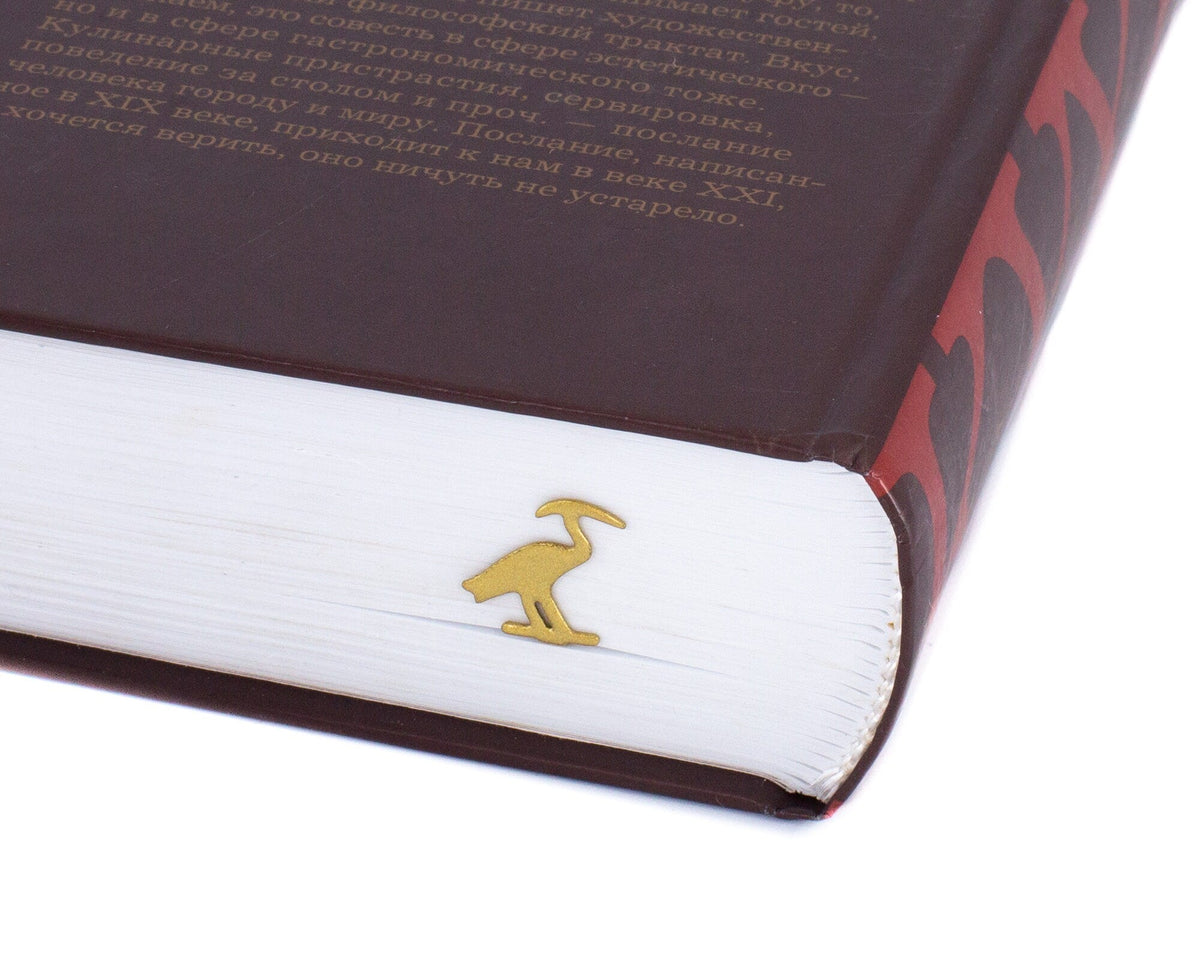 The Sacred Ibis metal bookmark in gold in a closed book, only its top showing above the pages