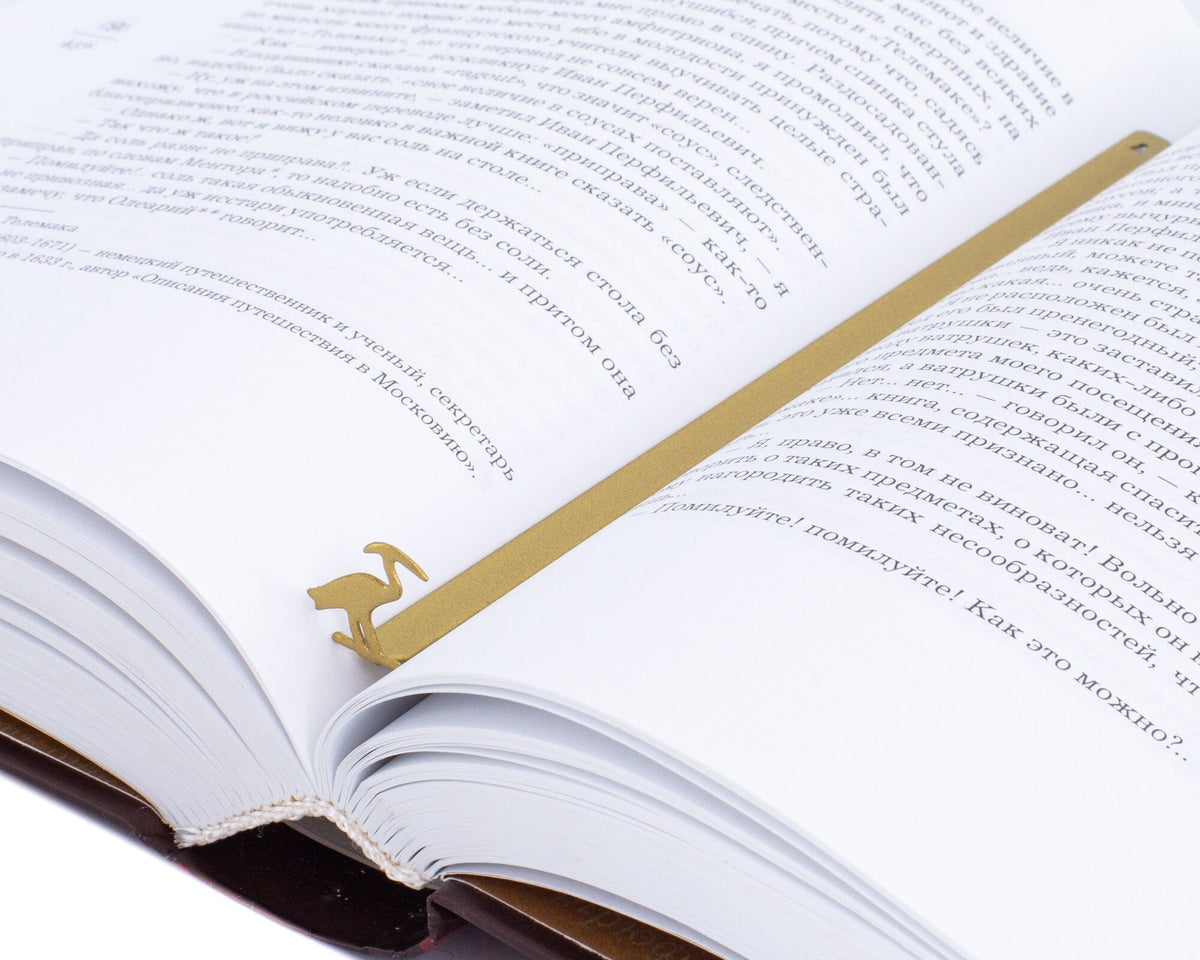 The Sacred Ibis metal bookmark in gold marking a page in an open book