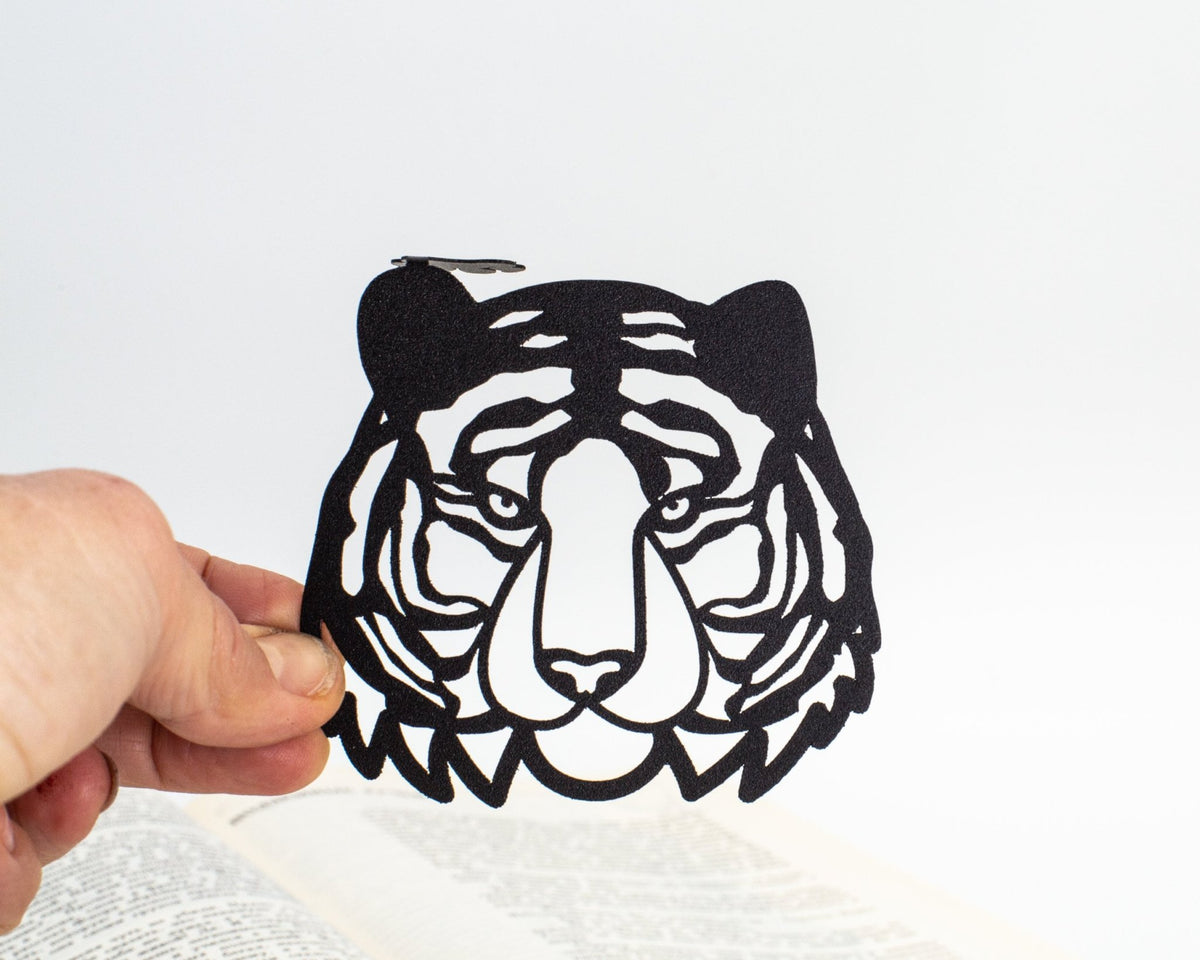 Tiger Head metal bookmark held in a hand above an open book