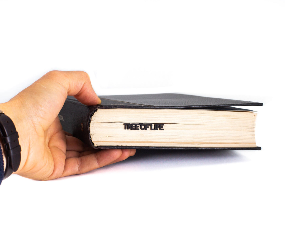 Tree of Life metal bookmark held in a hand above an open book