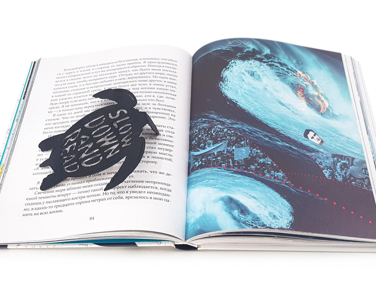Turtle metal bookmark marking a page in an illustrated book, view 4