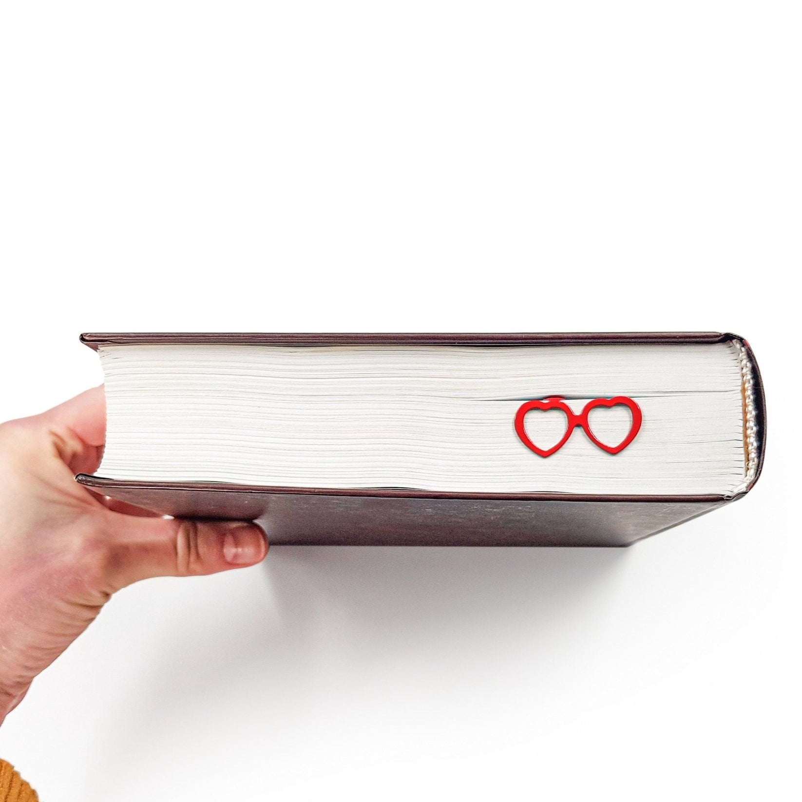 Vision Love metal bookmark in red held in a hand above an open book