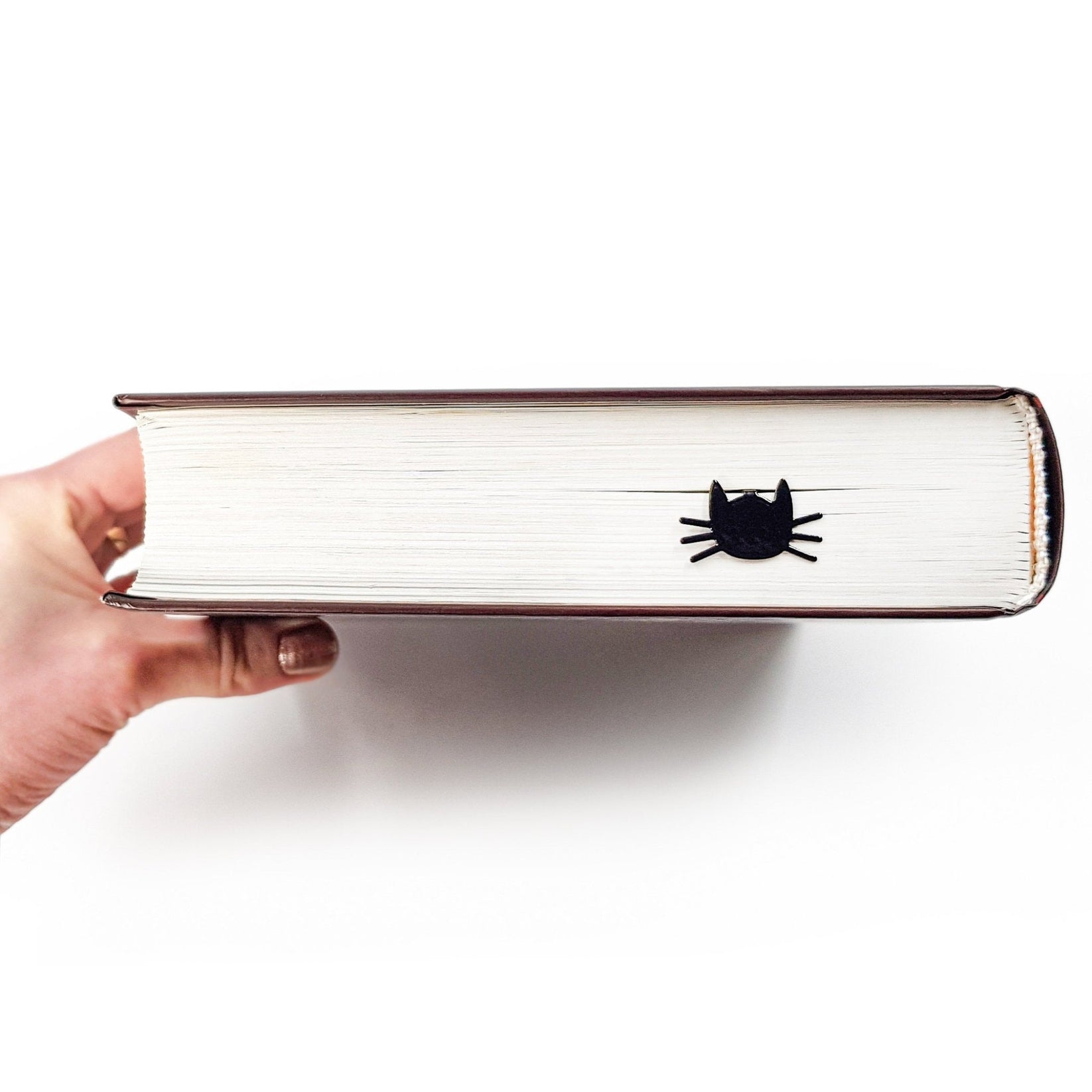 Whiskers in Your Book metal bookmark held in a hand above an open book