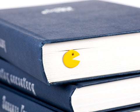 Yellow Monster metal bookmark in gold shown with a stack of books