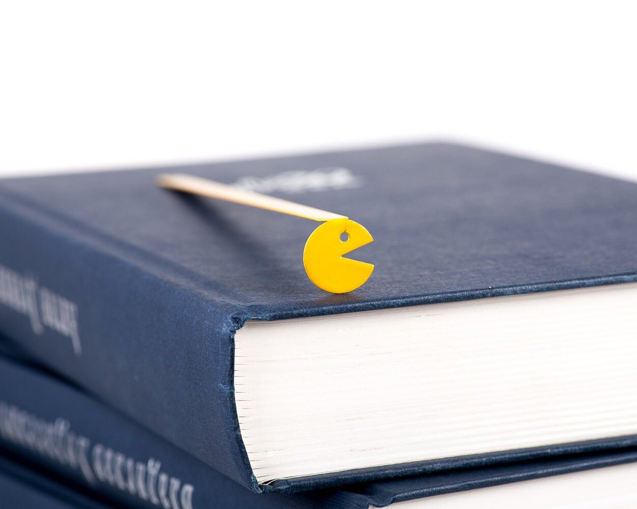 Yellow Monster metal bookmark in gold in a closed book, only its top showing above the pages