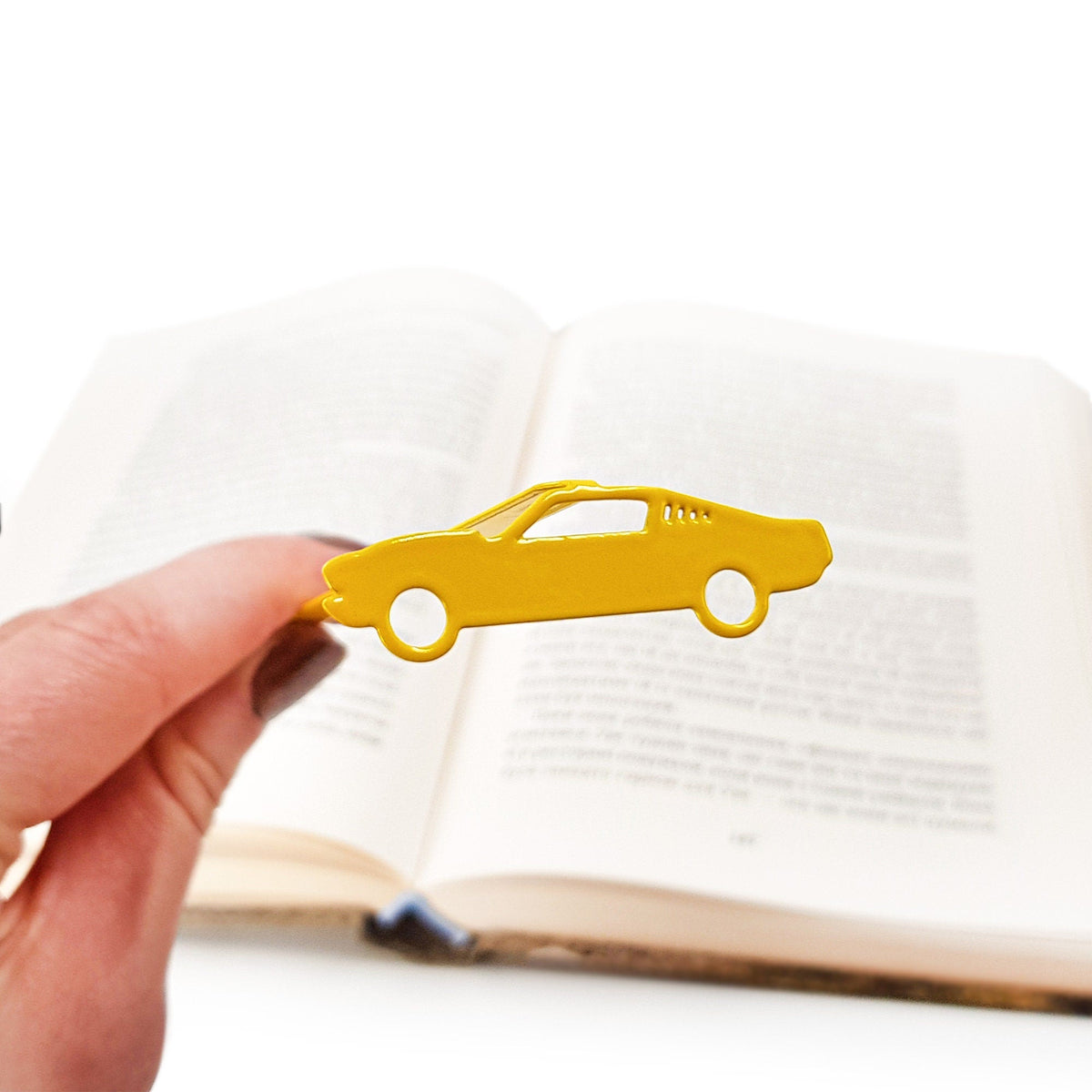 Yellow Muscle Car metal bookmark in gold held in a hand above an open book
