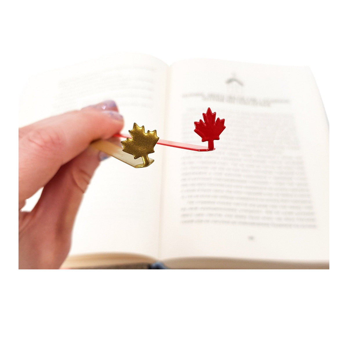 Canadian Maple Leaf metal bookmark in red held in a hand above an open book