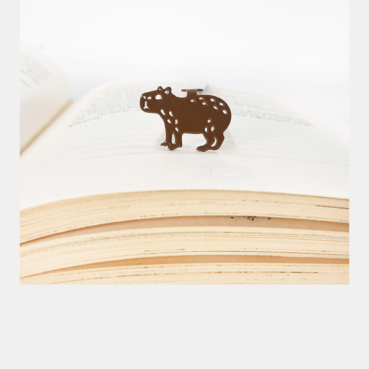 Capybara metal bookmark in a closed book, only its top showing above the pages