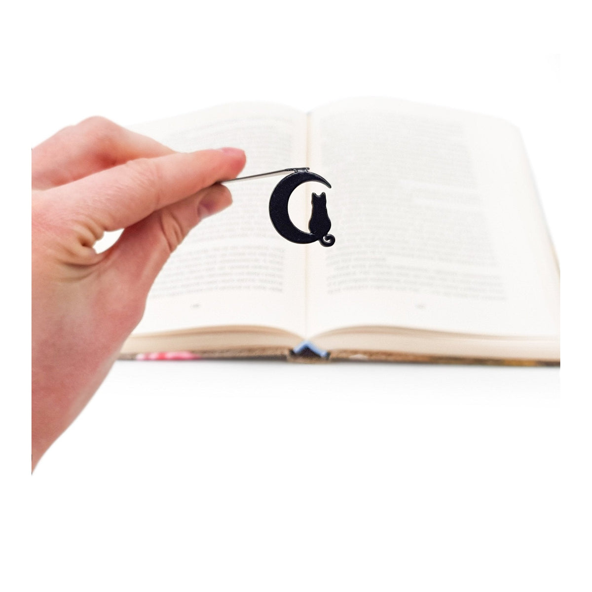 Cat on the Moon metal bookmark held in a hand above an open book