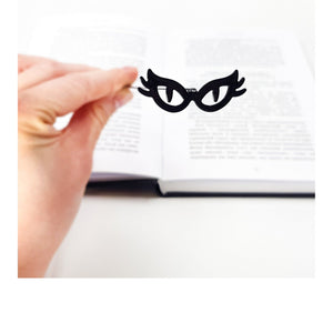 Cat’s Eye Glasses metal bookmark held in a hand above an open book