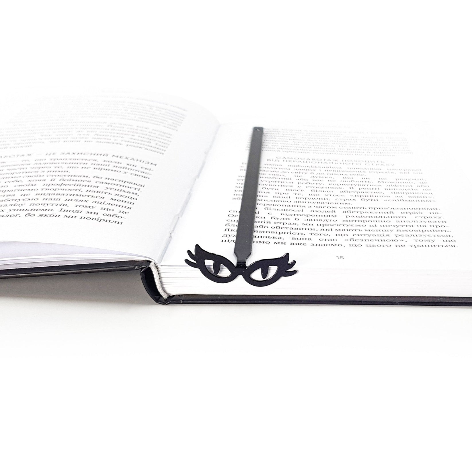 Black metal masquerade bookmark with cat’s eye glasses resting at the spine of an open book, minimalist bookish reading accessory