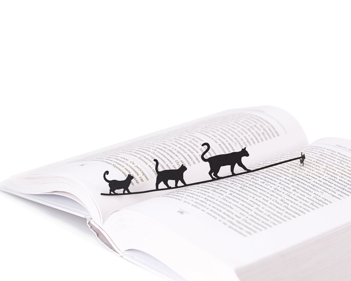 Cats Tightrope Walkers metal bookmark resting on the pages of an open book