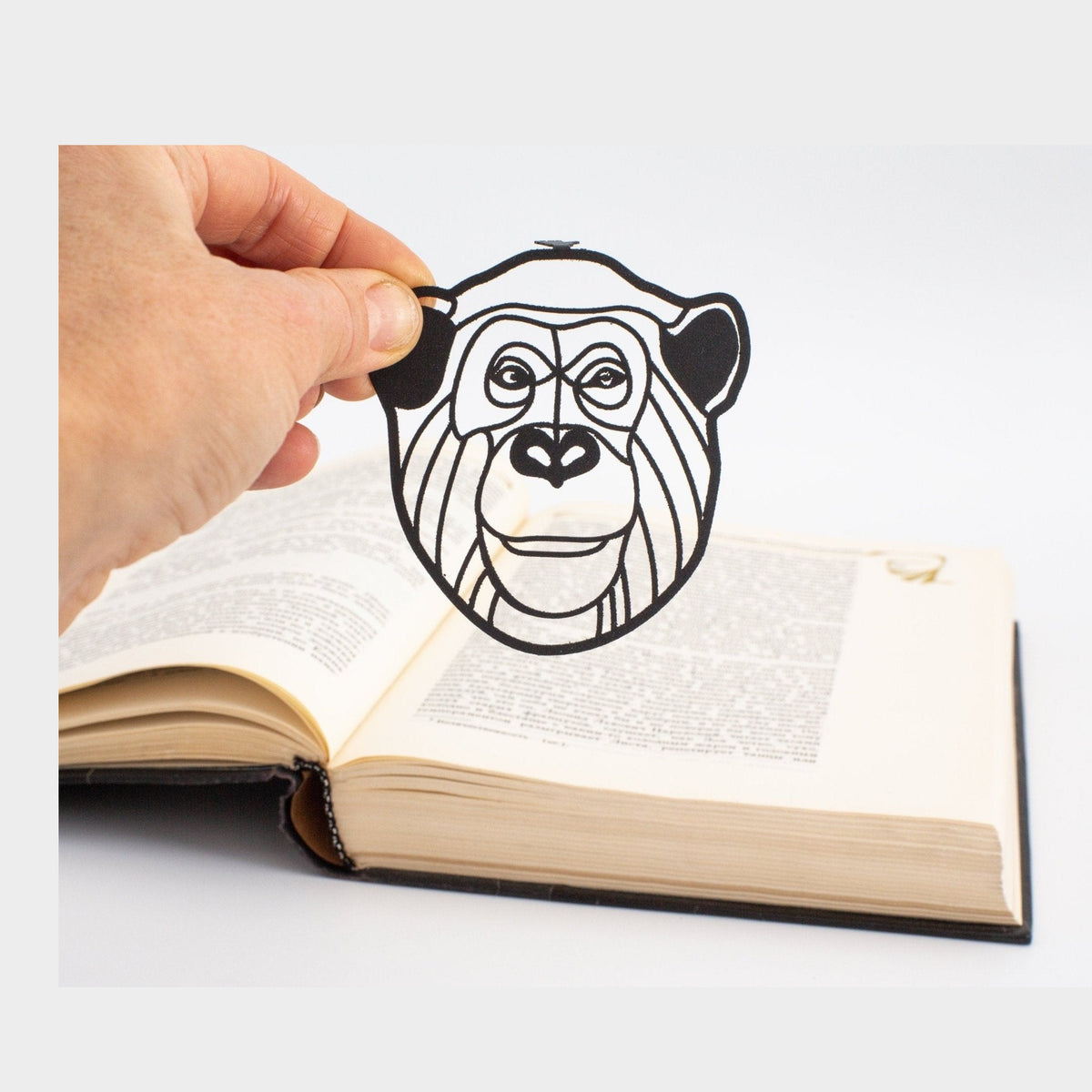 Chimp metal bookmark held in a hand above an open book
