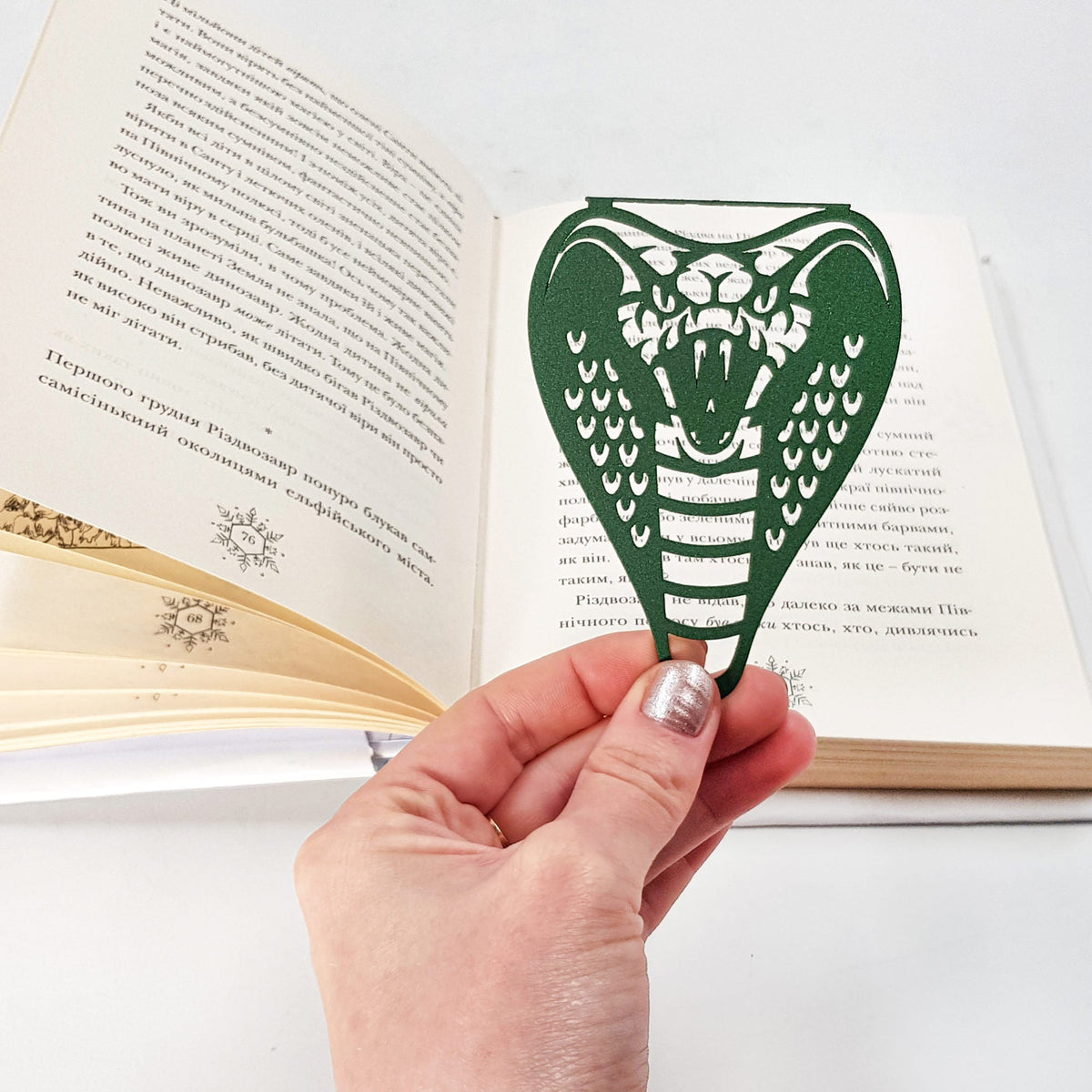 Cobra metal bookmark in green held in a hand above an open book