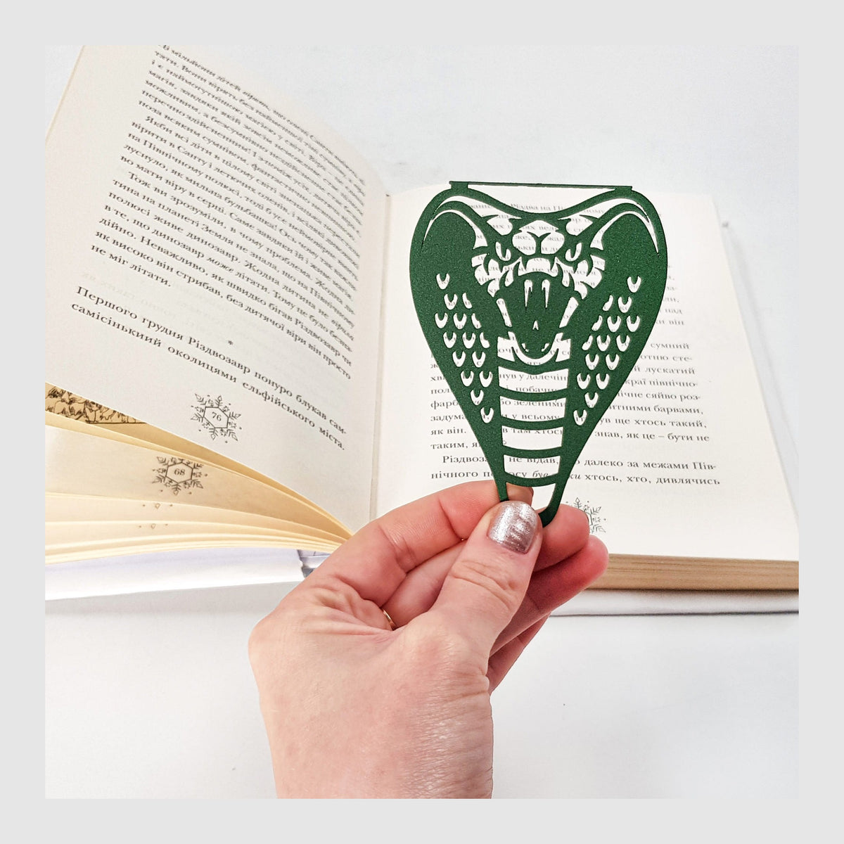 Cobra metal bookmark in green held in a hand above an open book