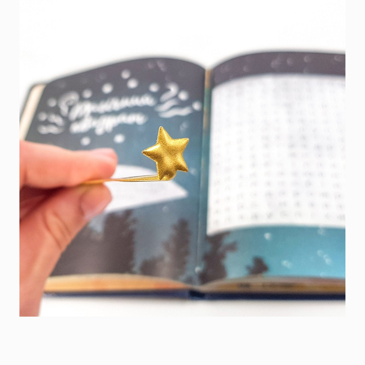 Comet metal bookmark in gold held in a hand above an open book