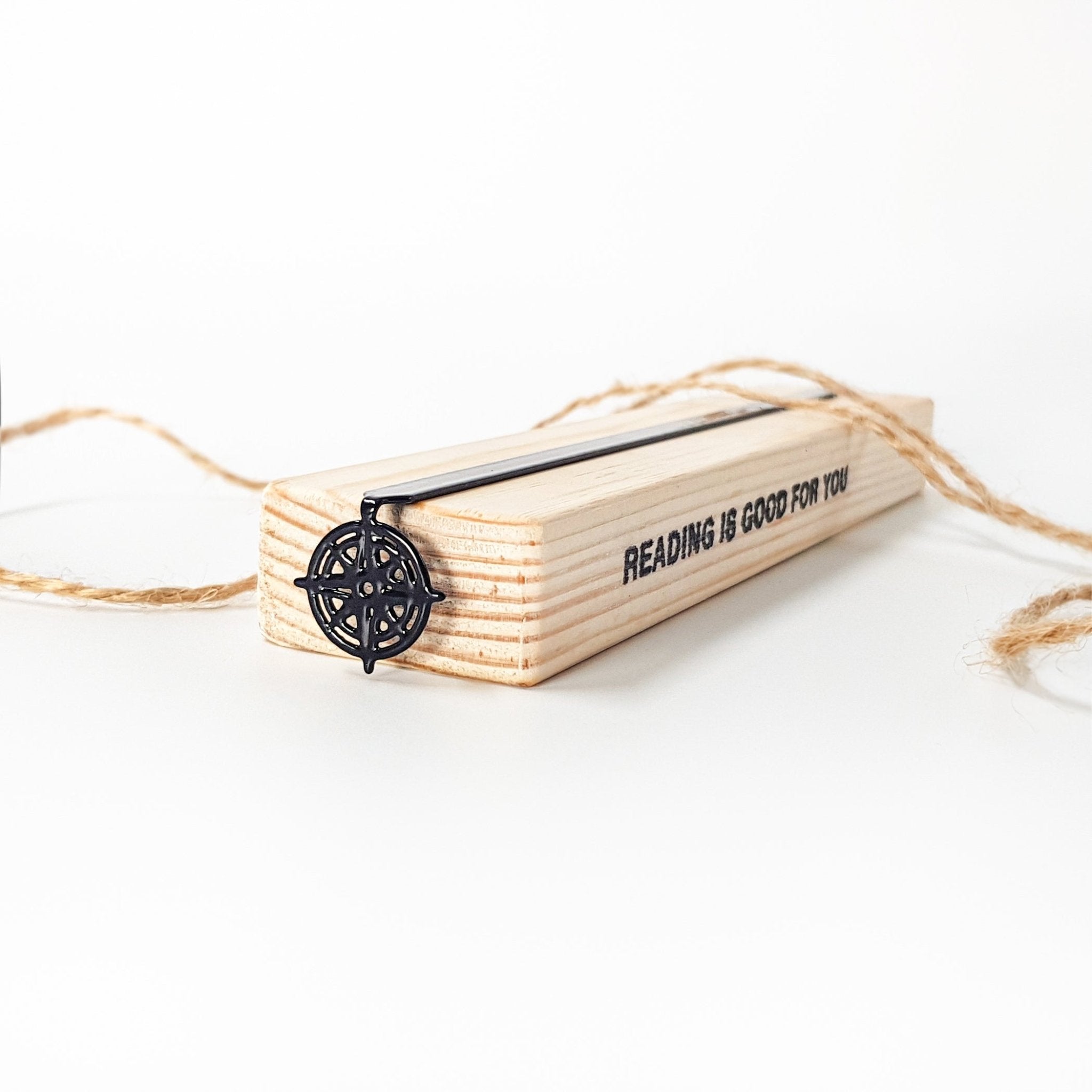 Black metal compass rose bookmark on wooden display block with twine — hero product shot