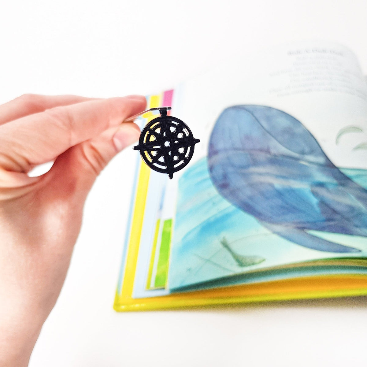 Compass Rose metal bookmark held in a hand above an open book