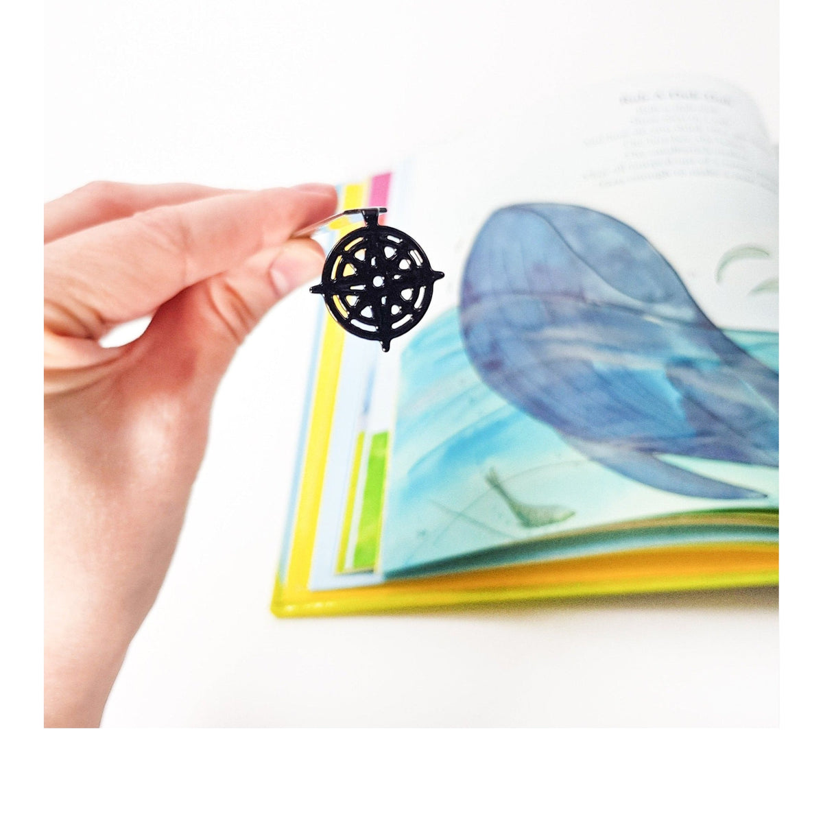 Compass Rose metal bookmark held in a hand above an open book