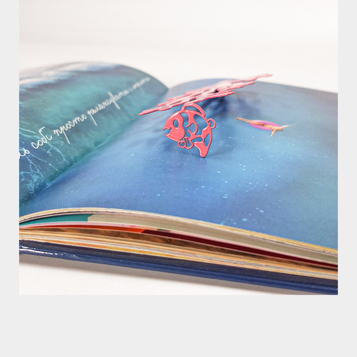 Corals metal bookmark in red marking a page in an illustrated book