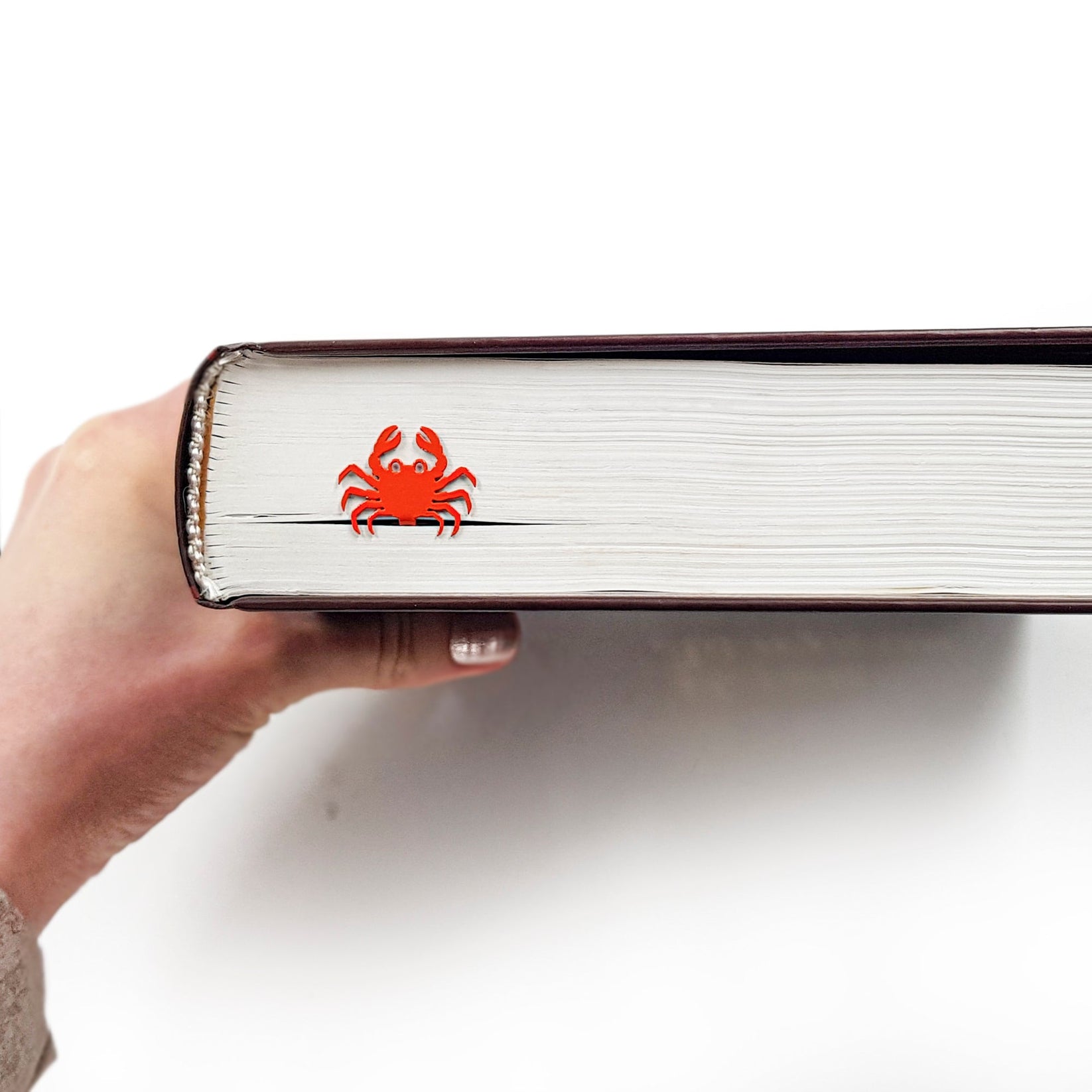 Crab metal bookmark in red in a closed book, only its top showing above the pages