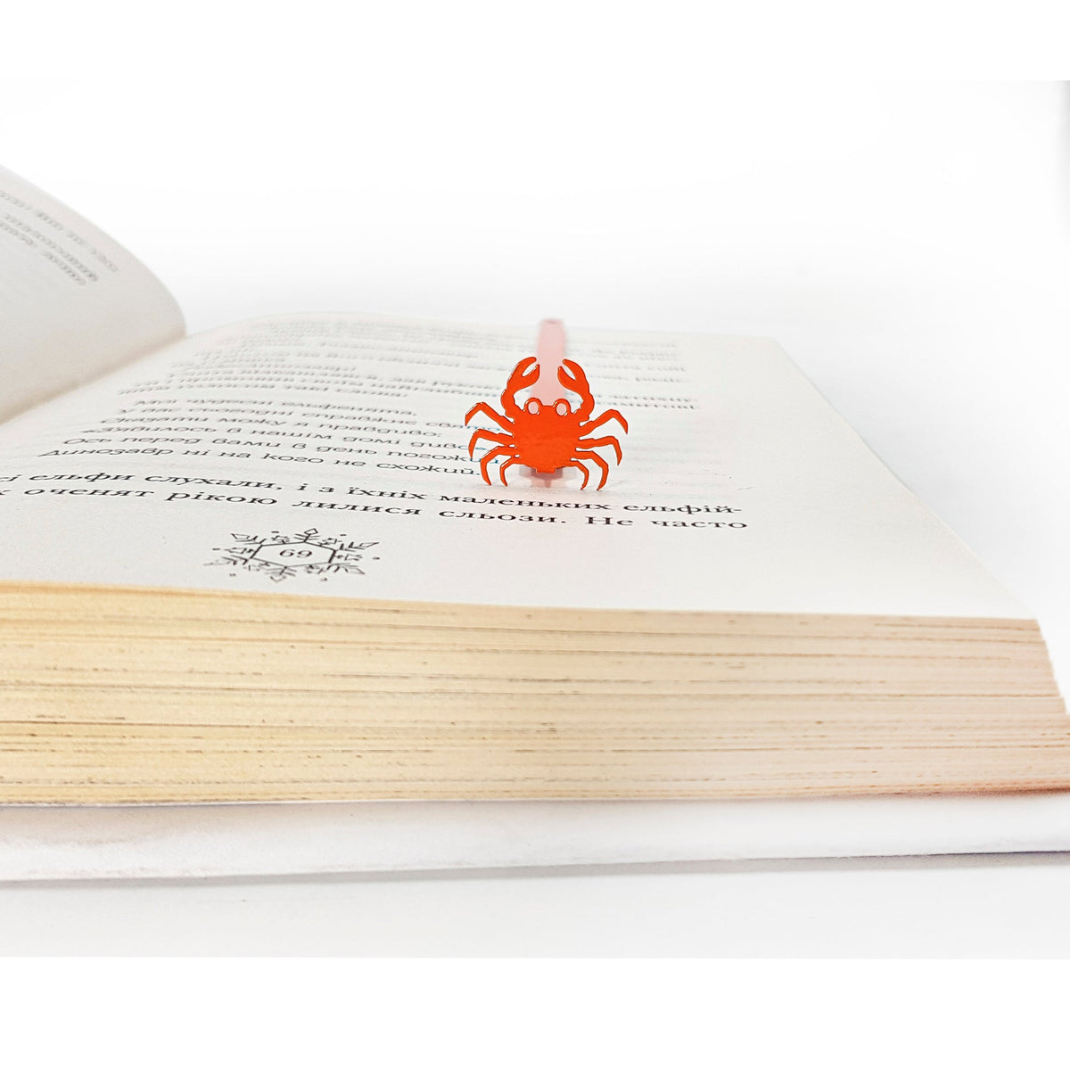 Crab metal bookmark in red seen from the edge of a closed book