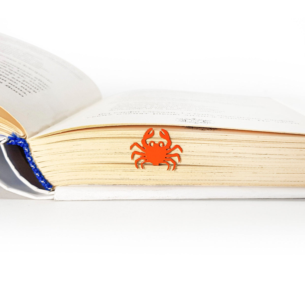 Crab metal bookmark in red resting on the pages of an open book