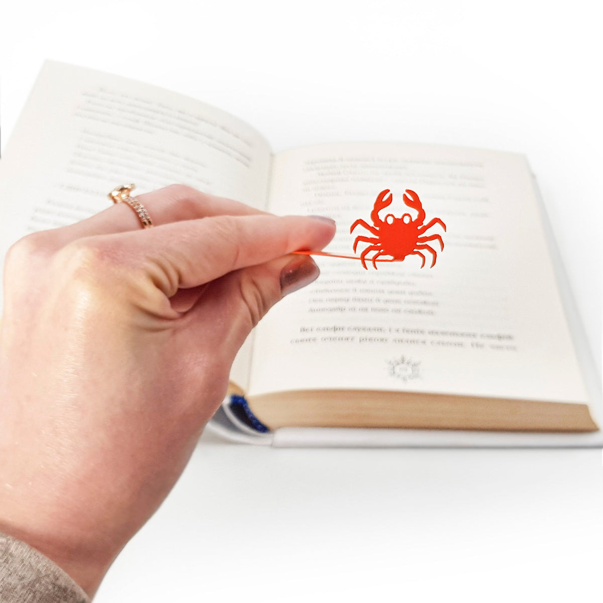 Crab metal bookmark in red held in a hand above an open book