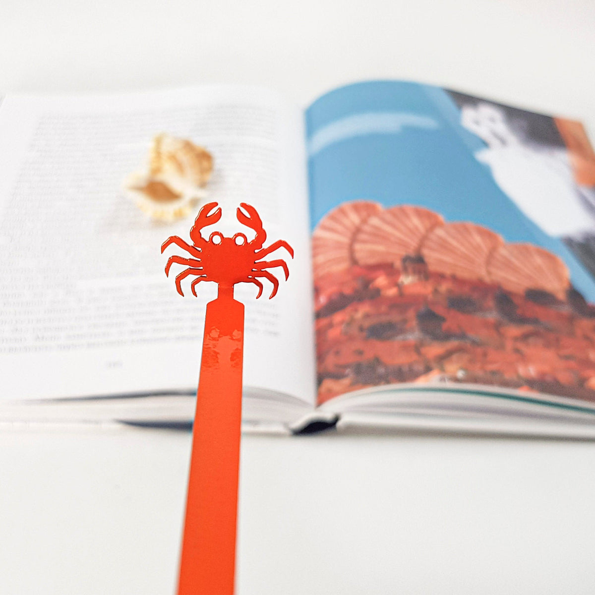Crab metal bookmark in red placed on a colour illustration