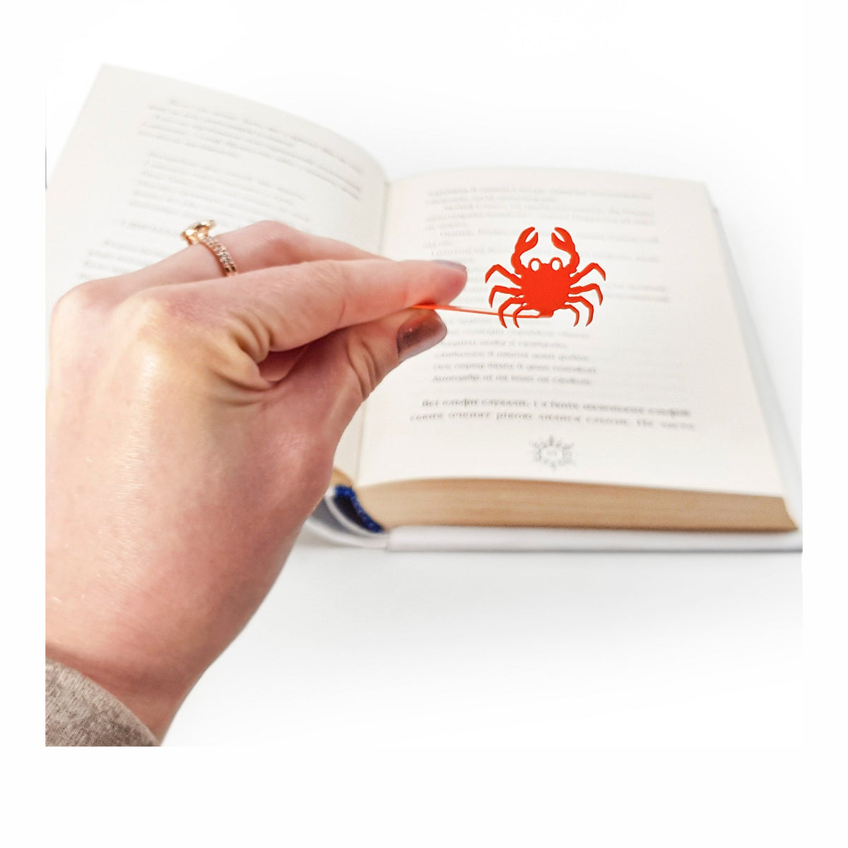 Crab metal bookmark in red held in a hand above an open book