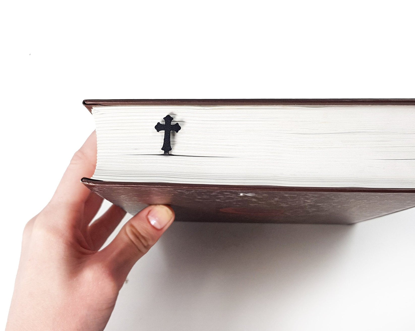 Cross metal bookmark seen from the edge of a closed book