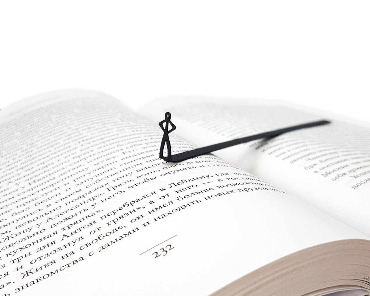 Black Stick Man metal bookmark marking a page in an open book