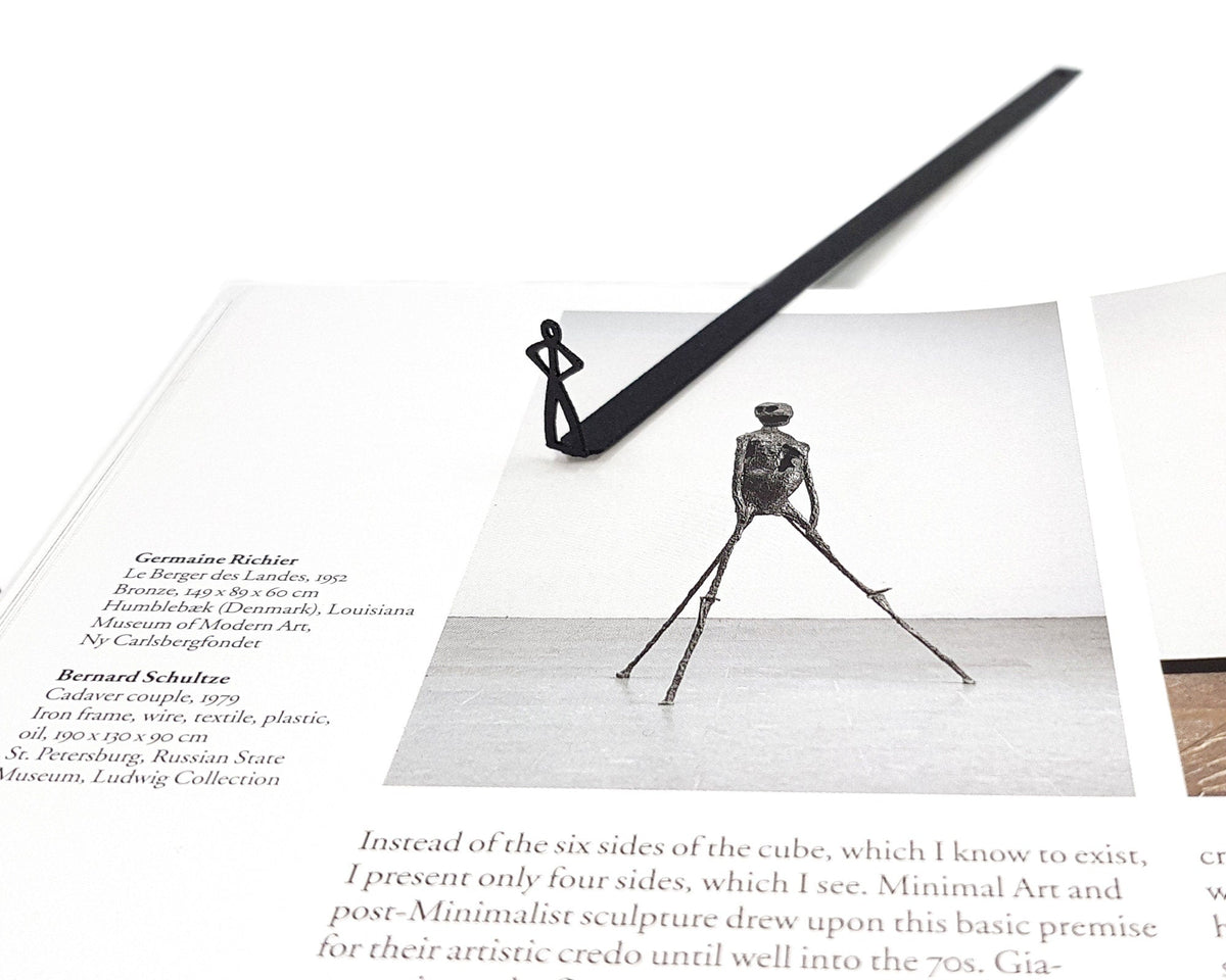 Black Stick Man metal bookmark marking a page in an illustrated book