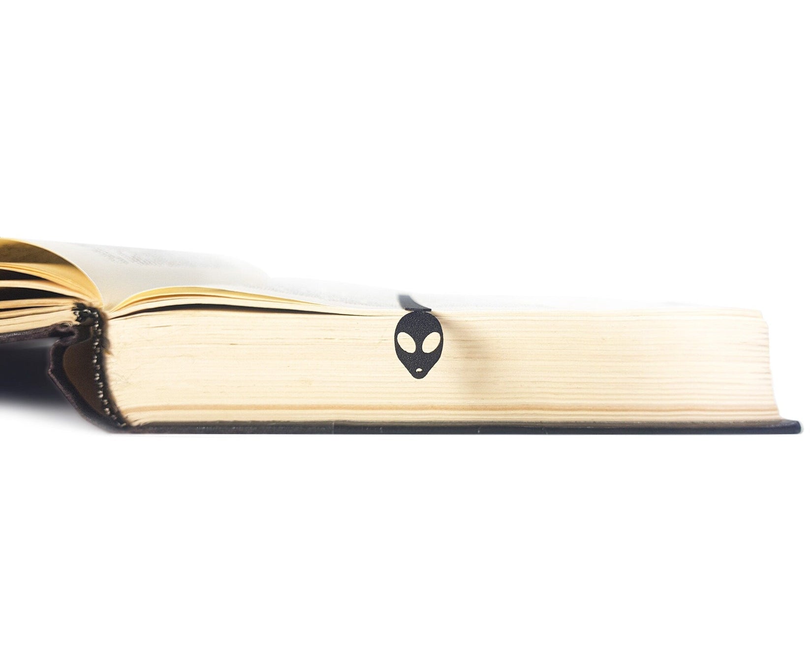 Alien Head metal bookmark seen from the edge of a closed book