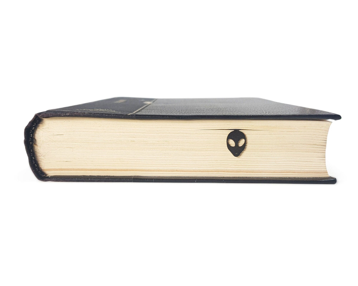 Alien Head metal bookmark in a closed book, only its top showing above the pages