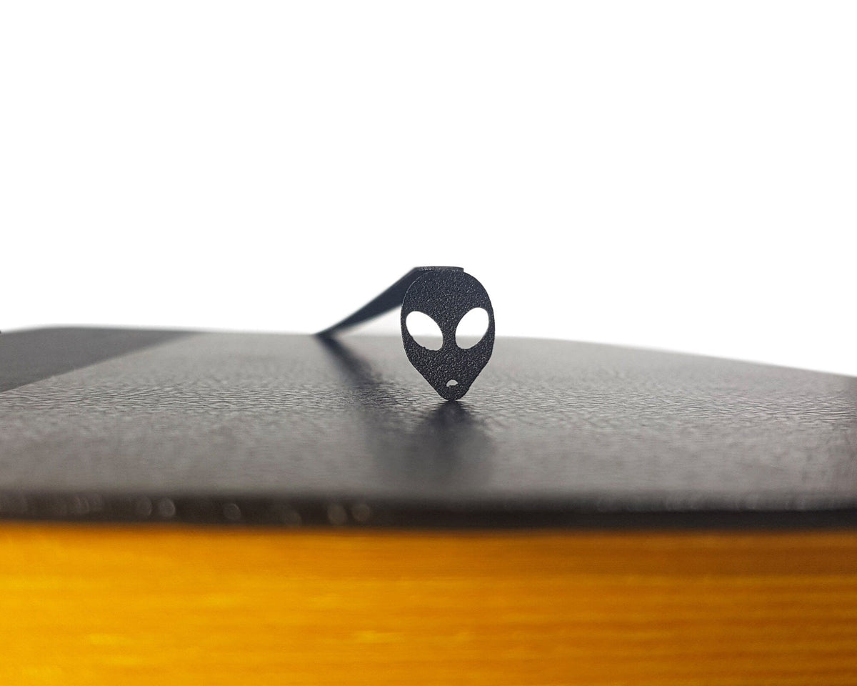 Alien Head metal bookmark clipped in a closed book, viewed from the side